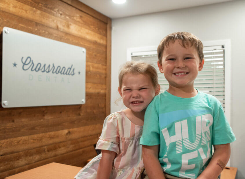 2 kids smiling in front of Crossroads Dental Sign